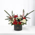 Elegant holiday floral arrangement in black box with red roses, white blooms, and evergreens.