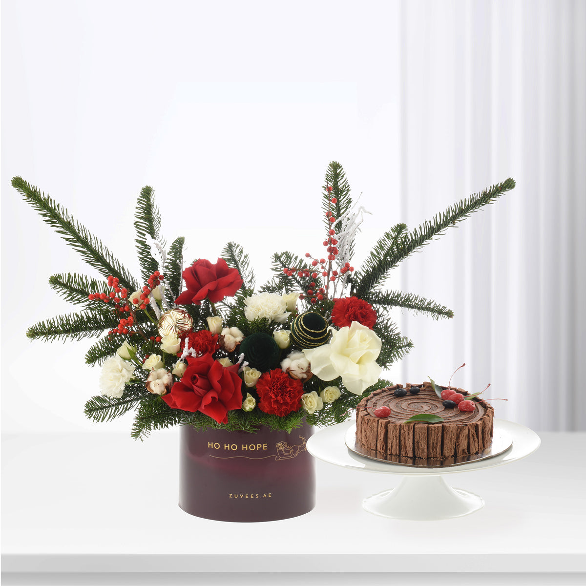 Festive red, white, green floral arrangement with pine, berries, and chocolate Yule log cake.