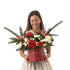 Woman holds festive red box with evergreens, red roses, white blooms, and berries.