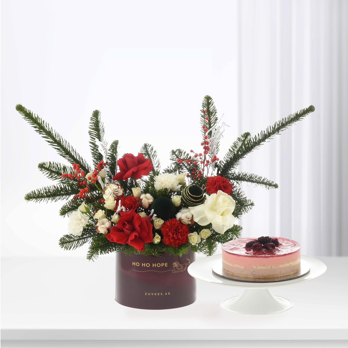 Elegant red and white floral arrangement with pine, berries, and cake on white stand.