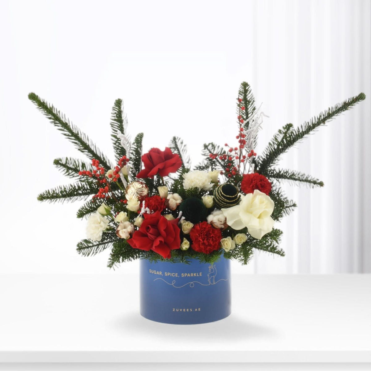 Vibrant red and white blooms nestled in festive greenery within a blue cylindrical container.
