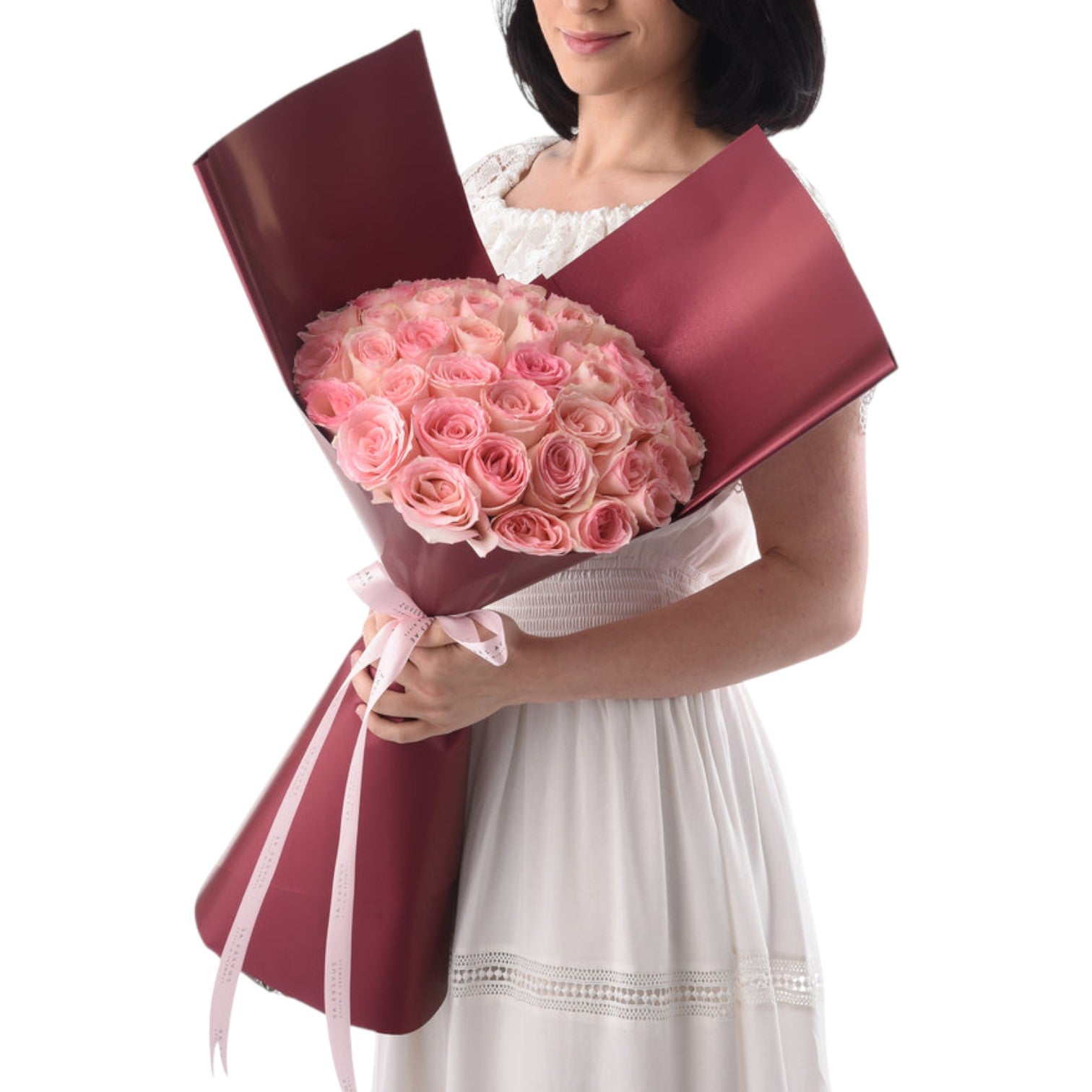 Woman holds lush pink rose bouquet in rich burgundy wrap with delicate pink ribbon.