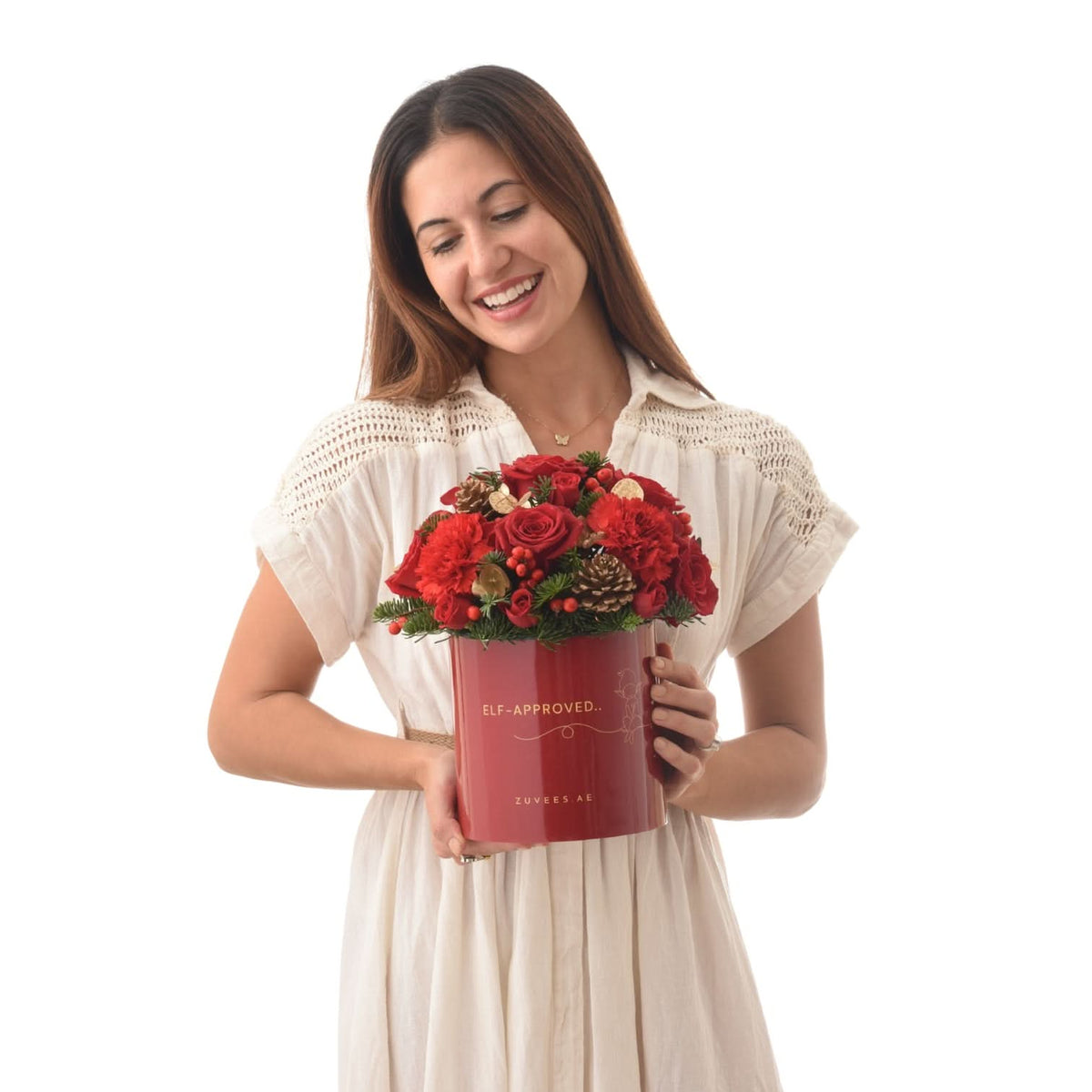 Woman smiles holding festive red floral arrangement in branded holiday tin.