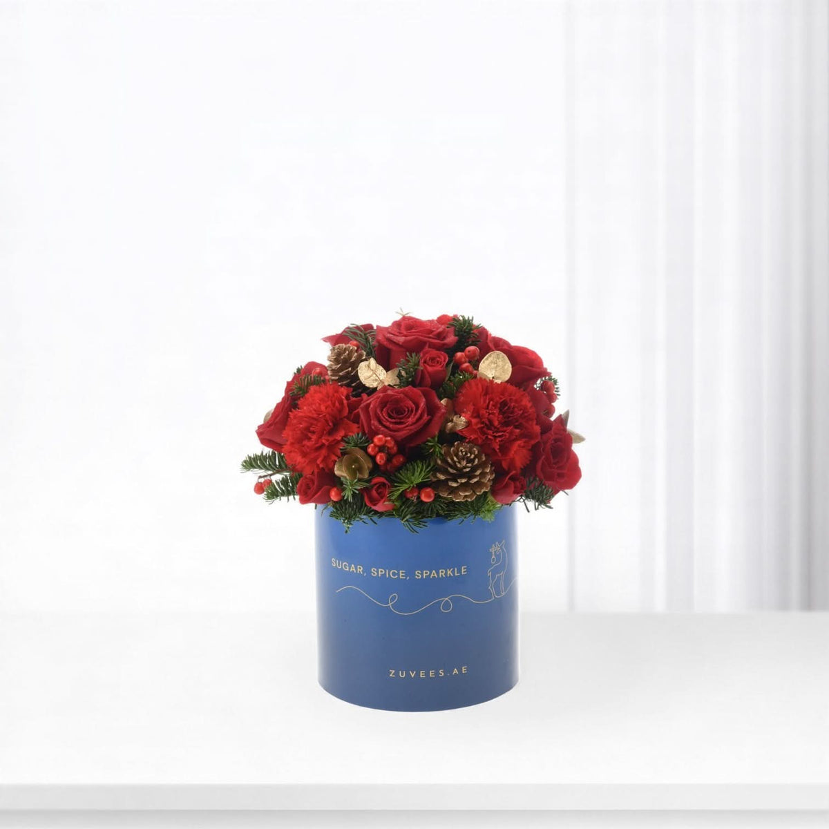 Vibrant red roses and berries in festive blue box with gold text.