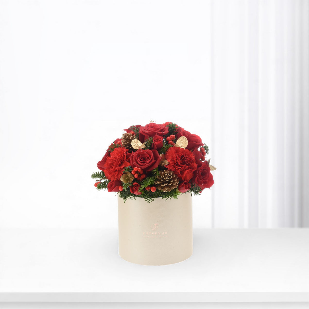 Vibrant red roses and carnations in beige box with pinecones and berries.