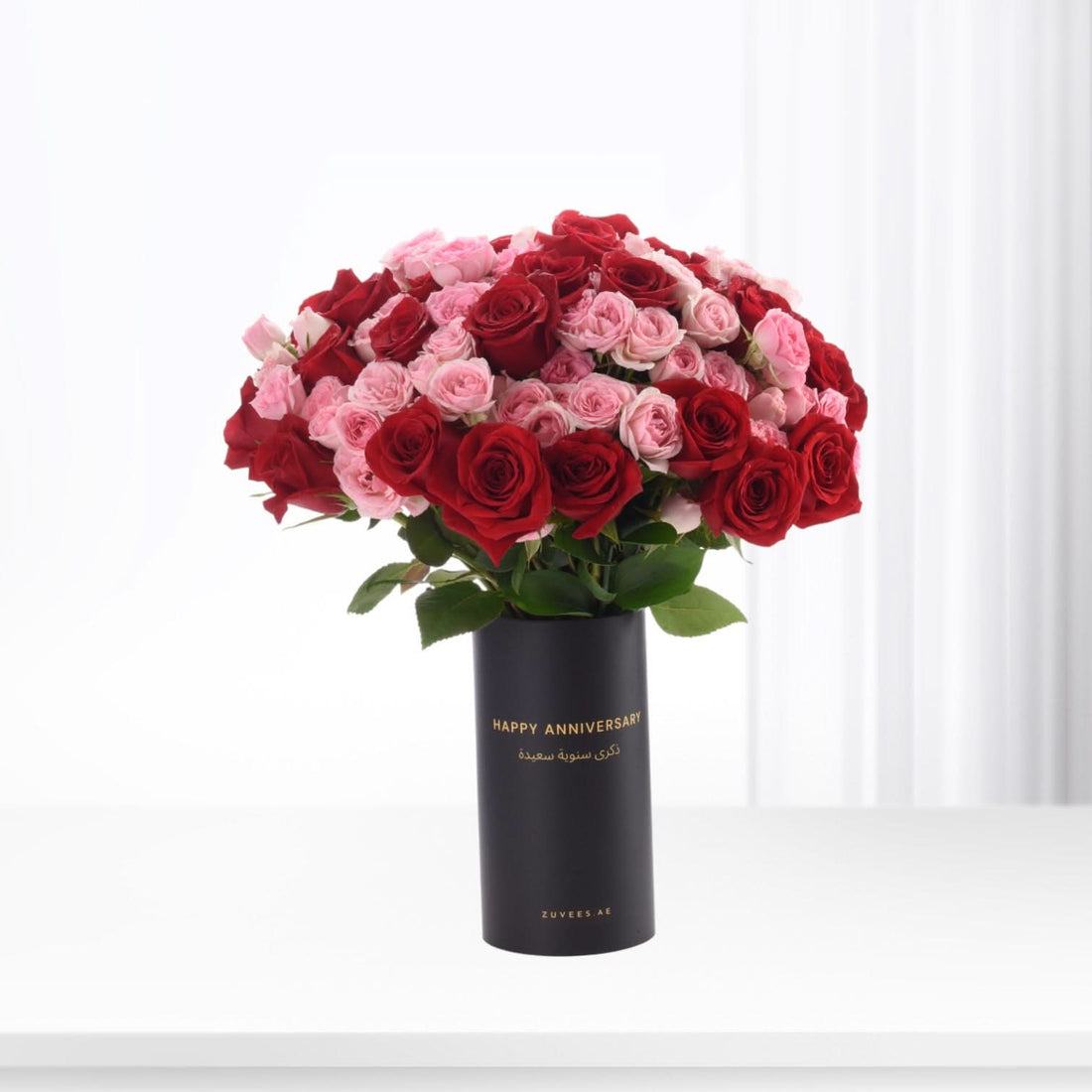 Bold red and blush pink roses in sleek black vase with gold "Happy Anniversary" text.