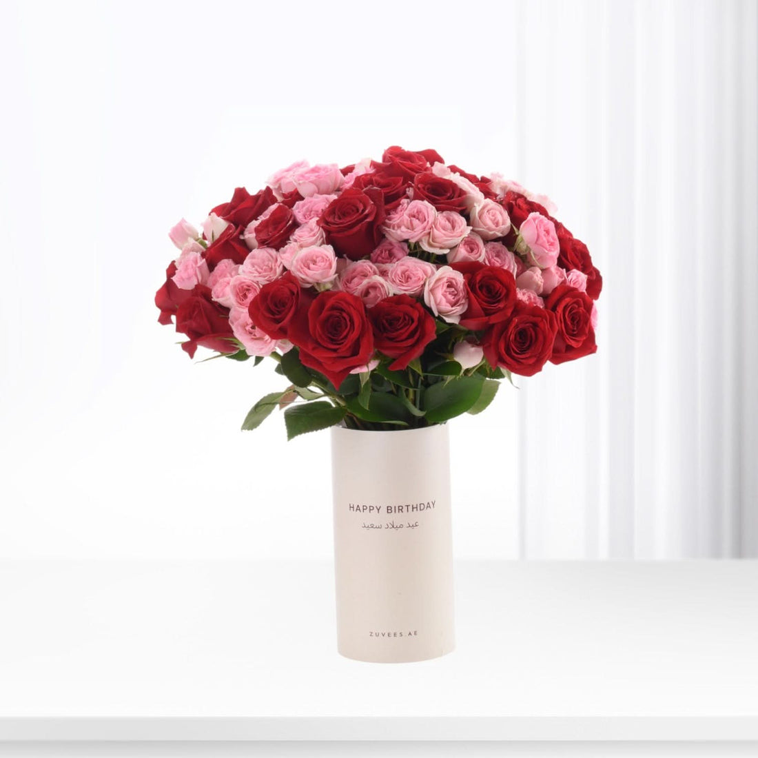 Vibrant red and pink roses in minimalist white vase with "Happy Birthday" text.