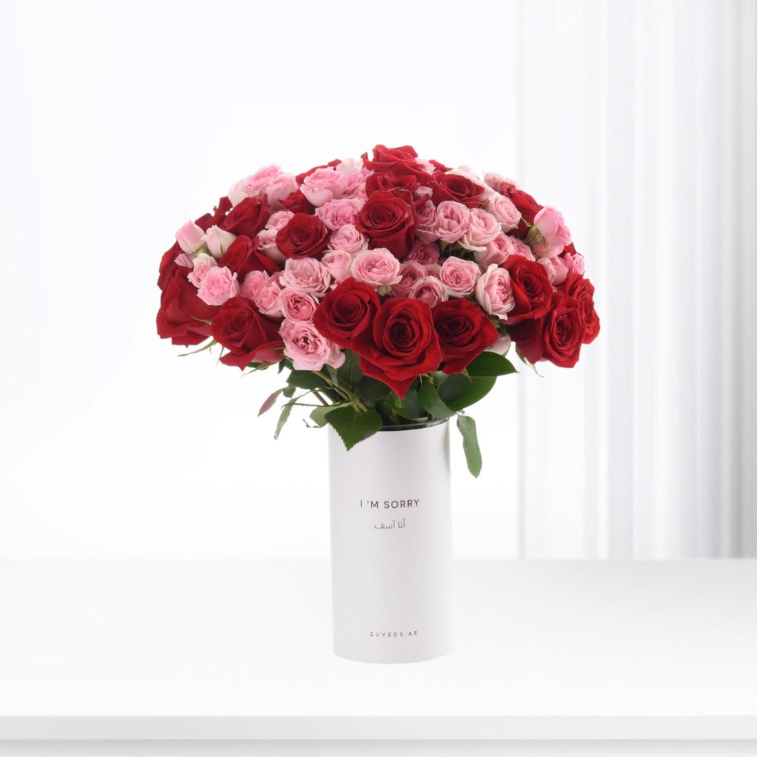 Vibrant red and pink roses in minimalist white vase with bilingual apology message.