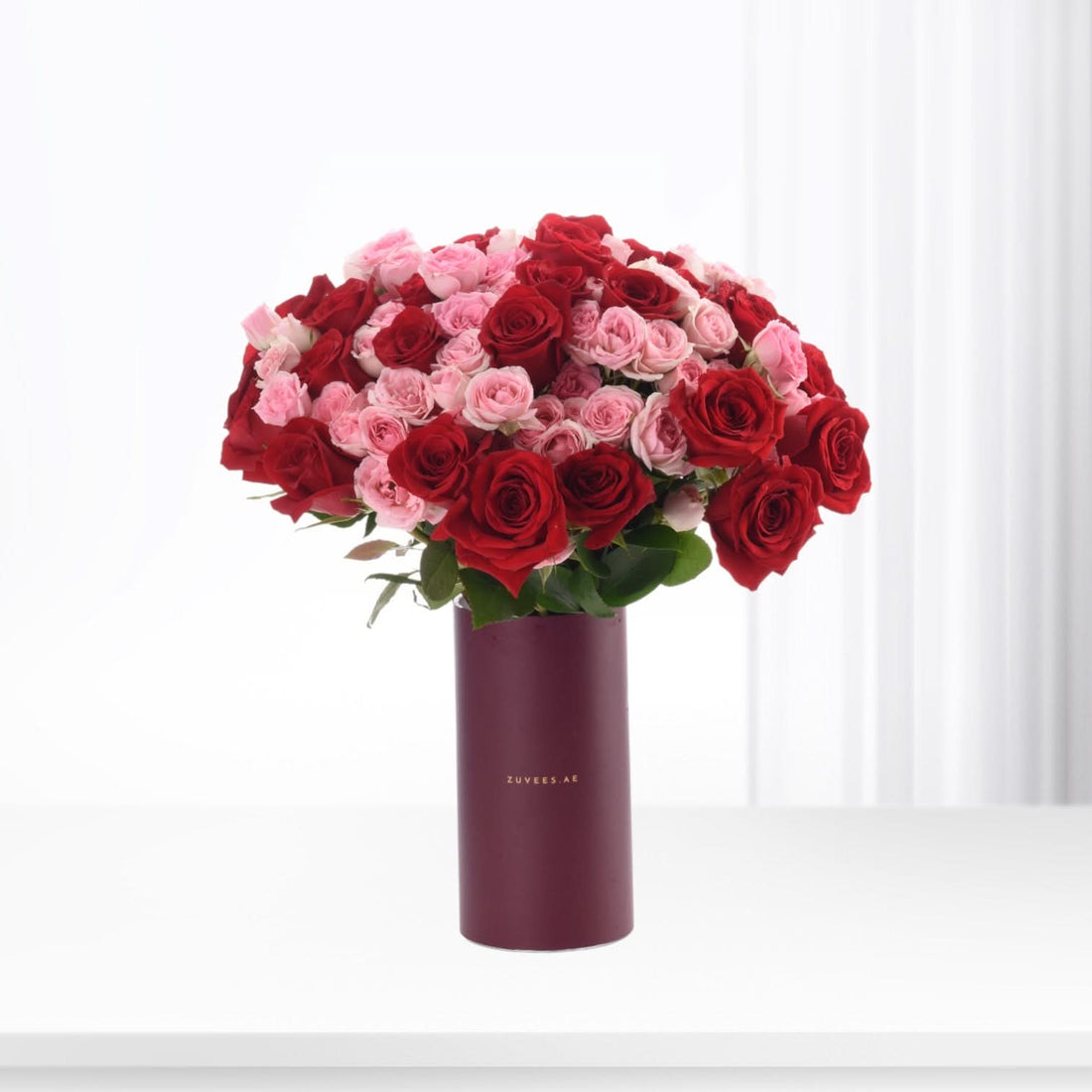 Vibrant red and pink roses in sleek burgundy vase, minimalist white backdrop.