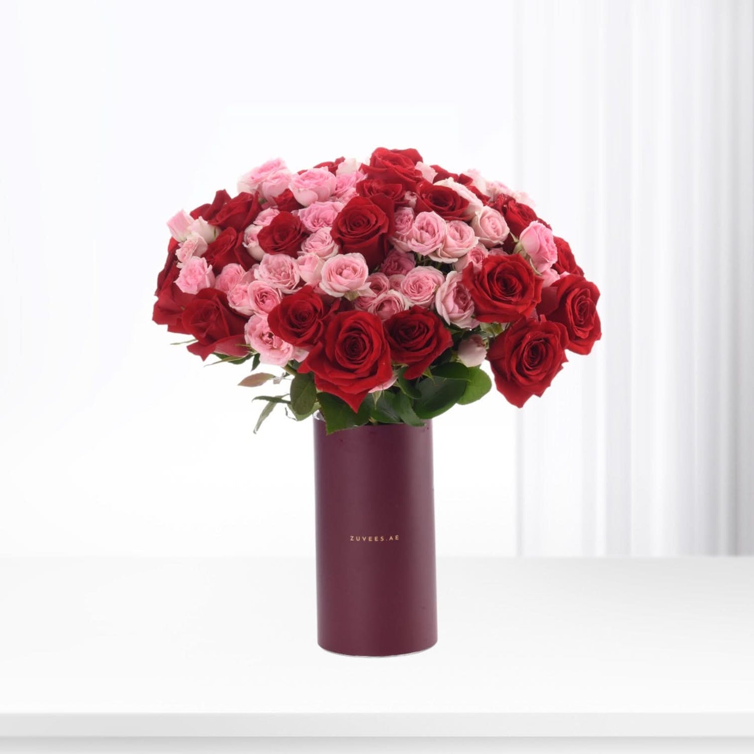 Vibrant red and pink roses in sleek burgundy vase, minimalist white backdrop.