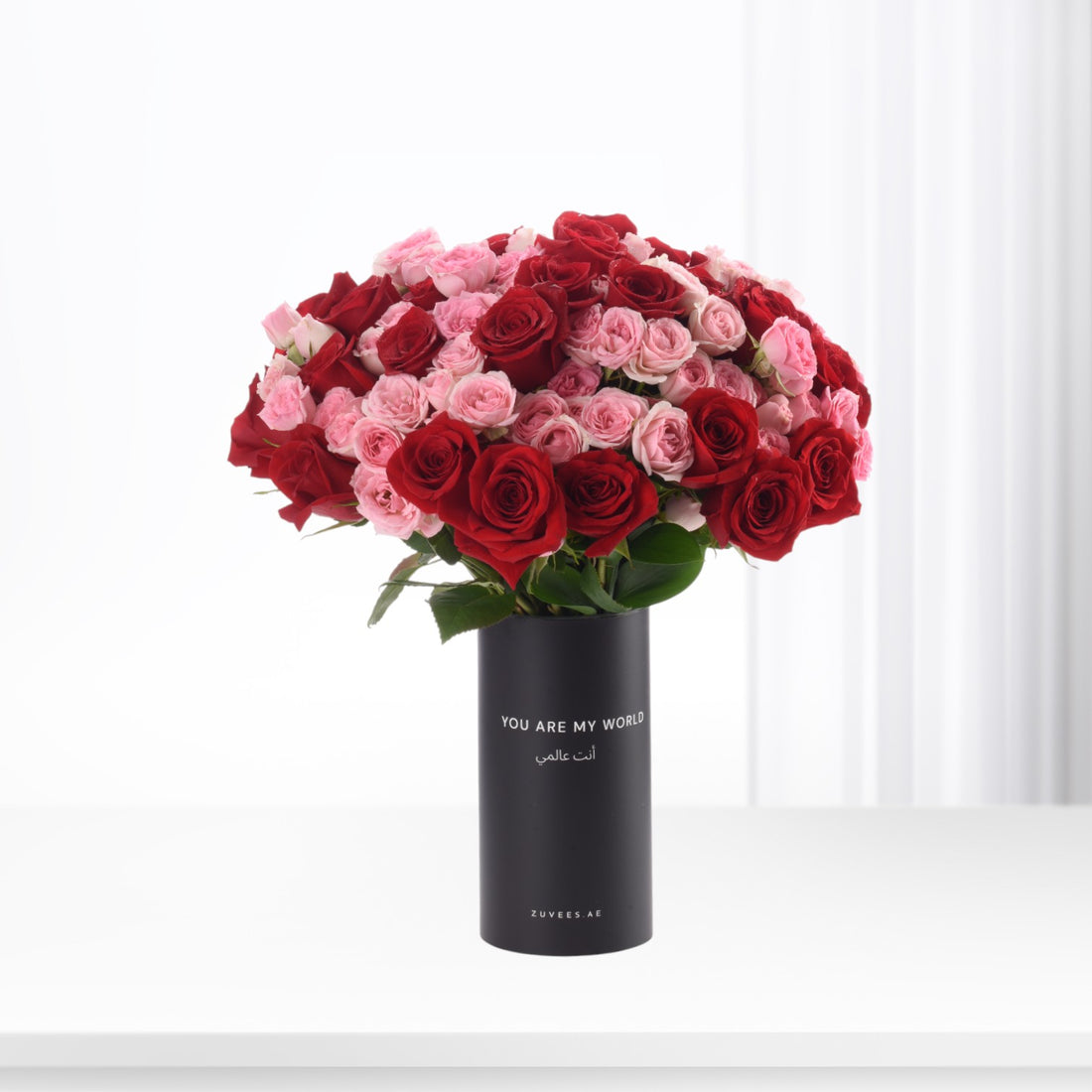 Vibrant red and pink roses in matte black vase with "You Are My World" text.