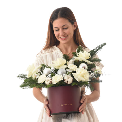 Woman smiles holding burgundy box with white flowers, greenery, and silver ornaments.