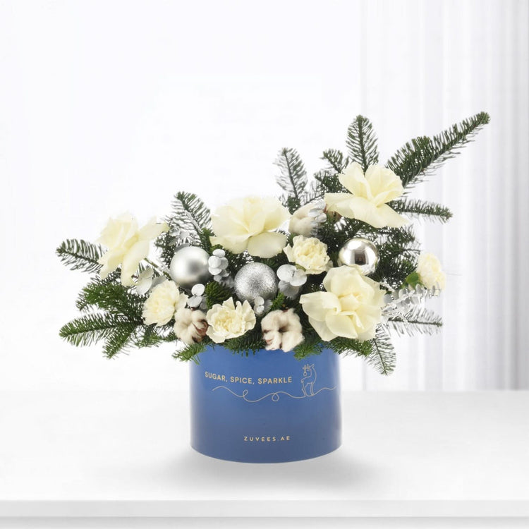 Blue vase holds white blooms, pine, cotton, silver ornaments—festive holiday arrangement.