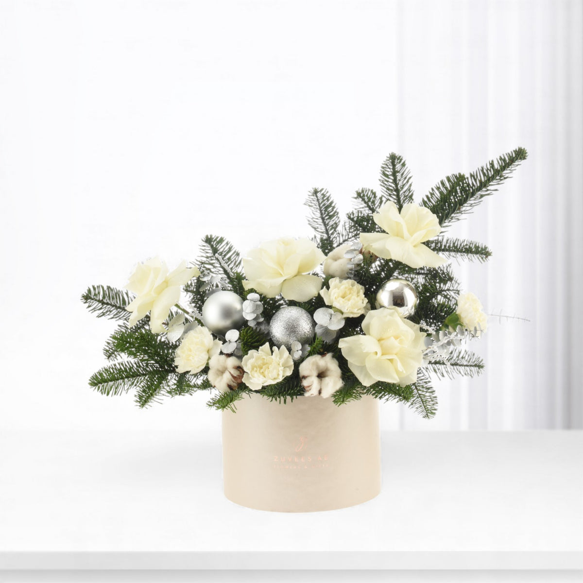 Elegant cream floral arrangement with silver ornaments in beige container.