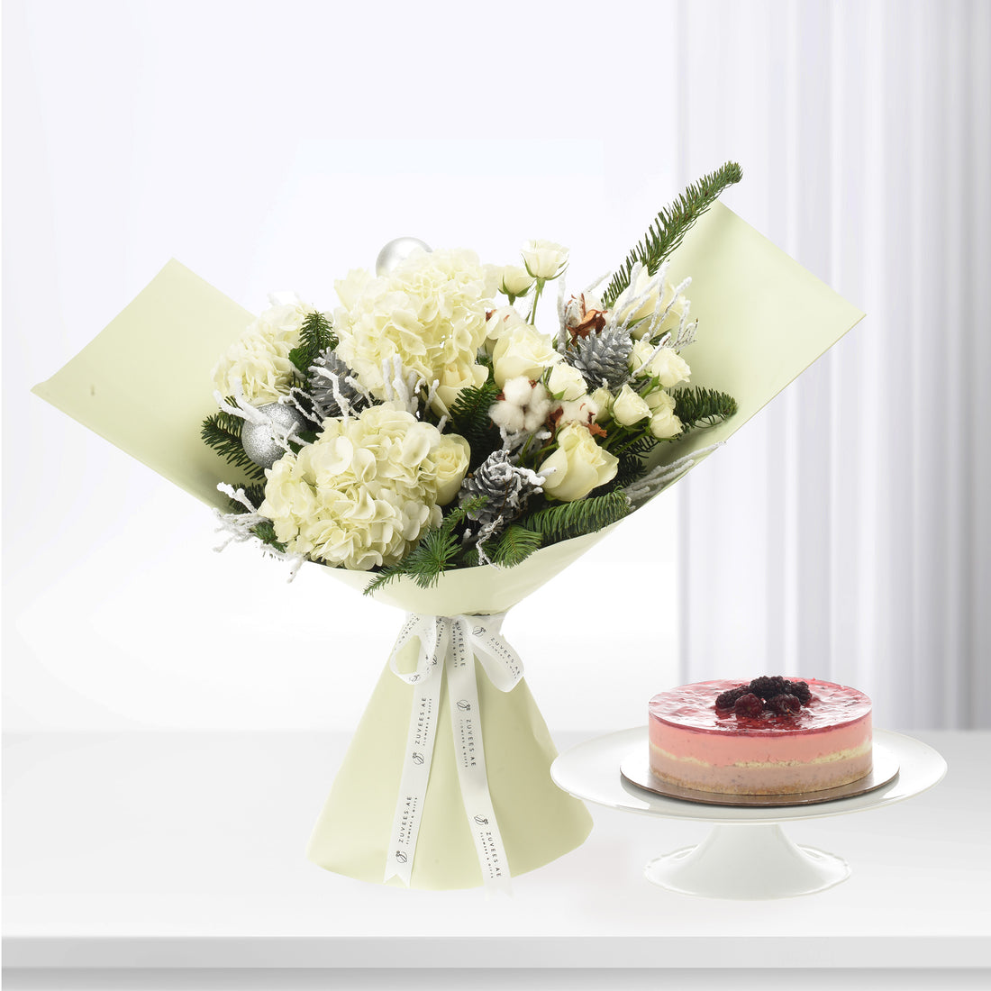 Elegant white hydrangea and rose bouquet with festive greenery, silver ornaments, paired with berry cheesecake.