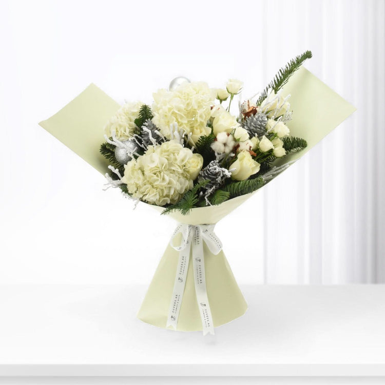 Elegant winter bouquet: white hydrangeas, roses, frosted pine, silver ornaments, pale green wrap, branded ribbon.
