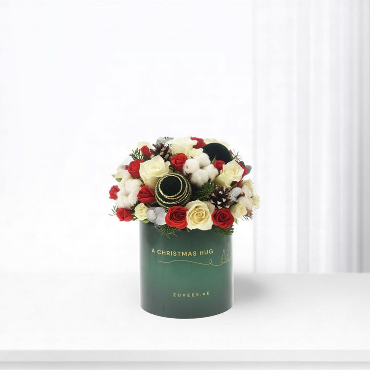 Festive red and white roses with pinecones, cotton, ornaments in green "A Christmas Hug" box.