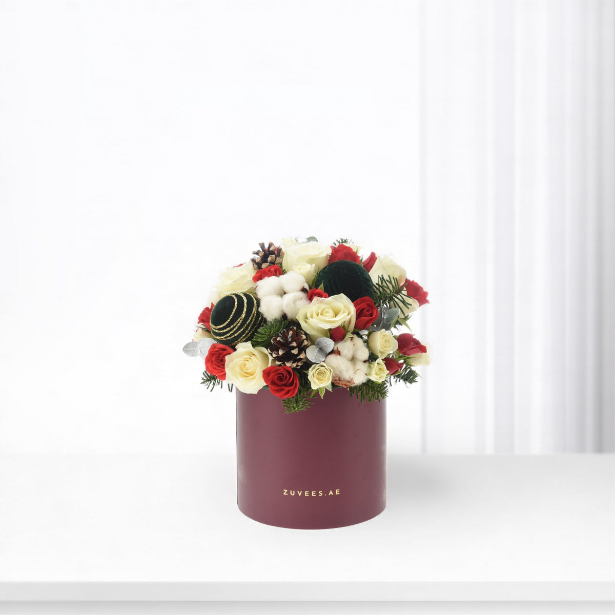 Elegant burgundy box holds red and cream roses, pinecones, and festive greenery.