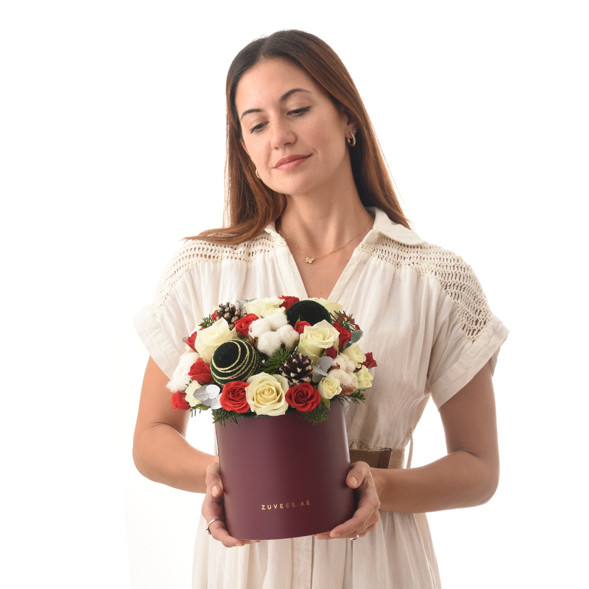 Woman holds burgundy box with red and white roses, pinecones, and cotton.
