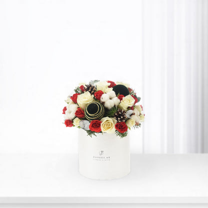 White box holds festive red and cream roses, cotton, pinecones, and ornaments.