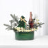 Elegant green Christmas gift basket with champagne, candle, and festive florals.