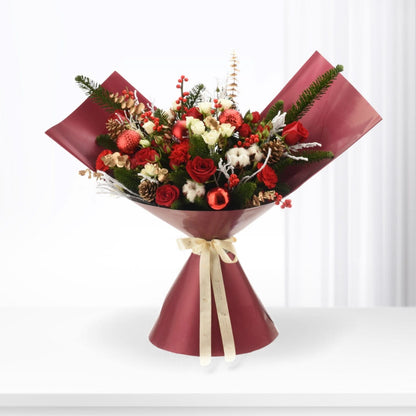 Vibrant red roses, pine, berries, and ornaments in glossy burgundy wrap with cream ribbon.