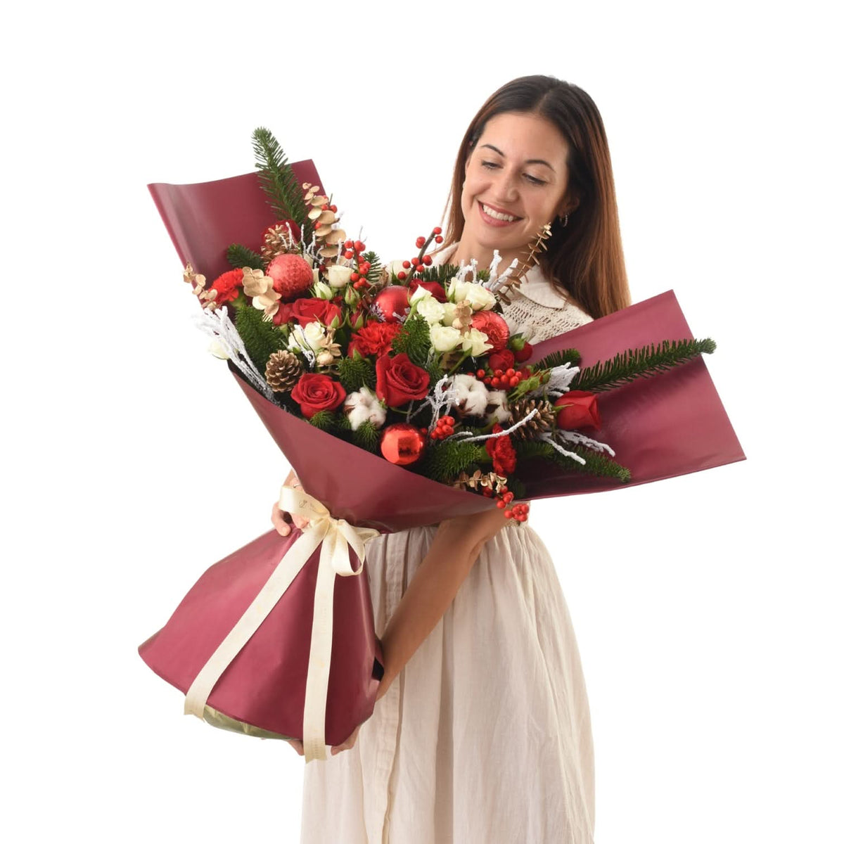Woman holds festive red-wrapped bouquet with roses, pine, berries, and pinecones.