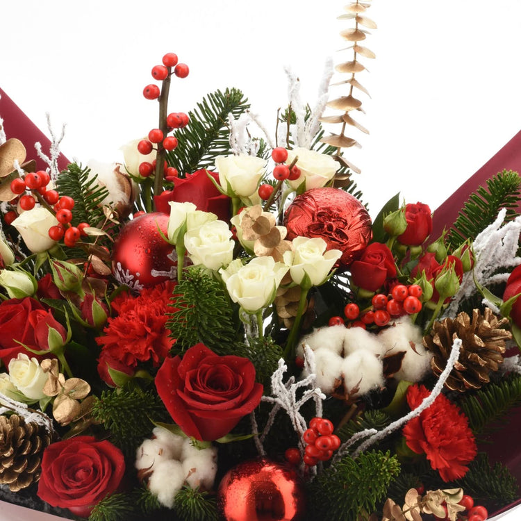 Vibrant red roses, white blooms, holly, pine, and glittering ornaments in festive holiday bouquet.