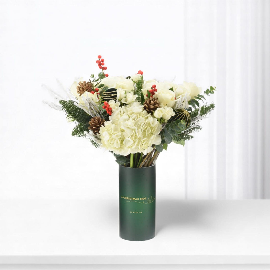 Elegant white floral arrangement in dark green vase with festive pine and berries.