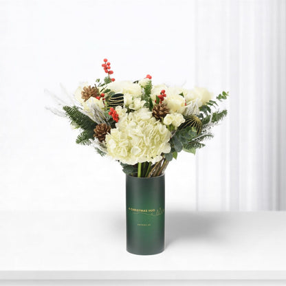 Elegant white floral arrangement in dark green vase with festive pine and berries.