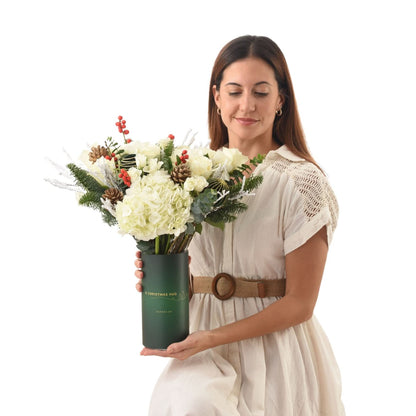 Woman holds festive white floral arrangement in dark green holiday vase.