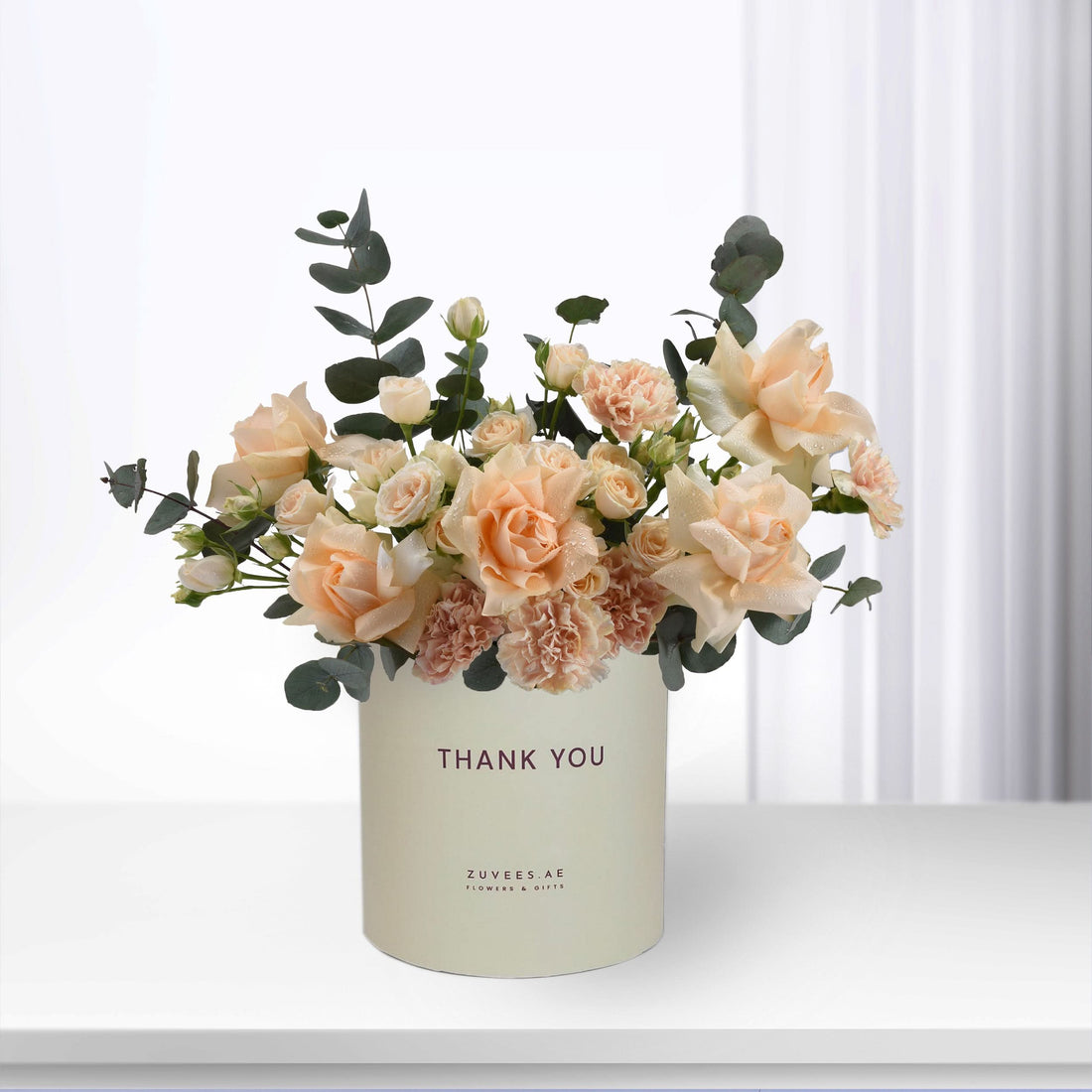 Soft peach roses and eucalyptus in cream vase with "Thank You" message.