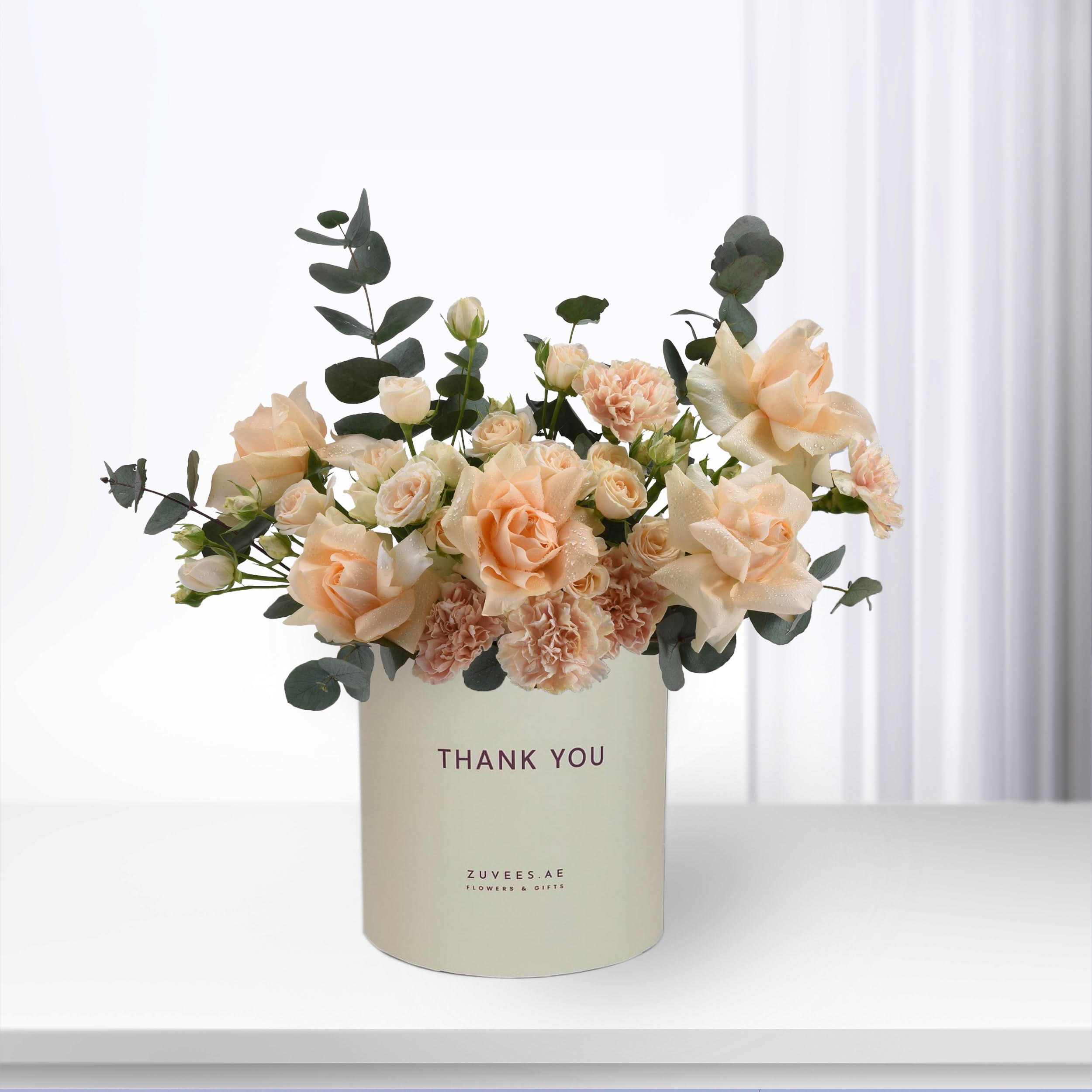Soft peach roses and eucalyptus in cream vase with "Thank You" message.