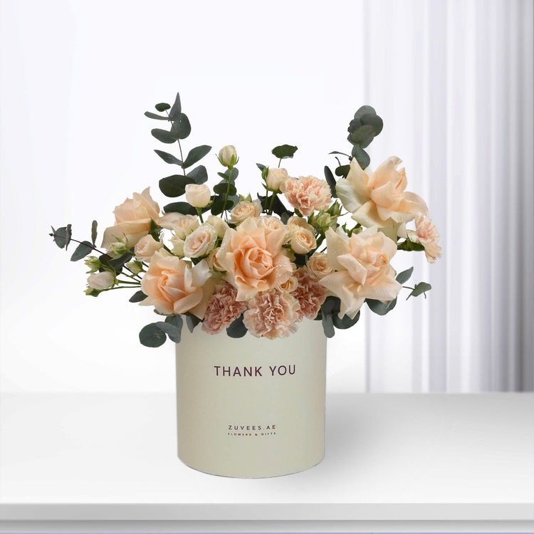 Soft peach roses and eucalyptus in cream vase with "Thank You" message.