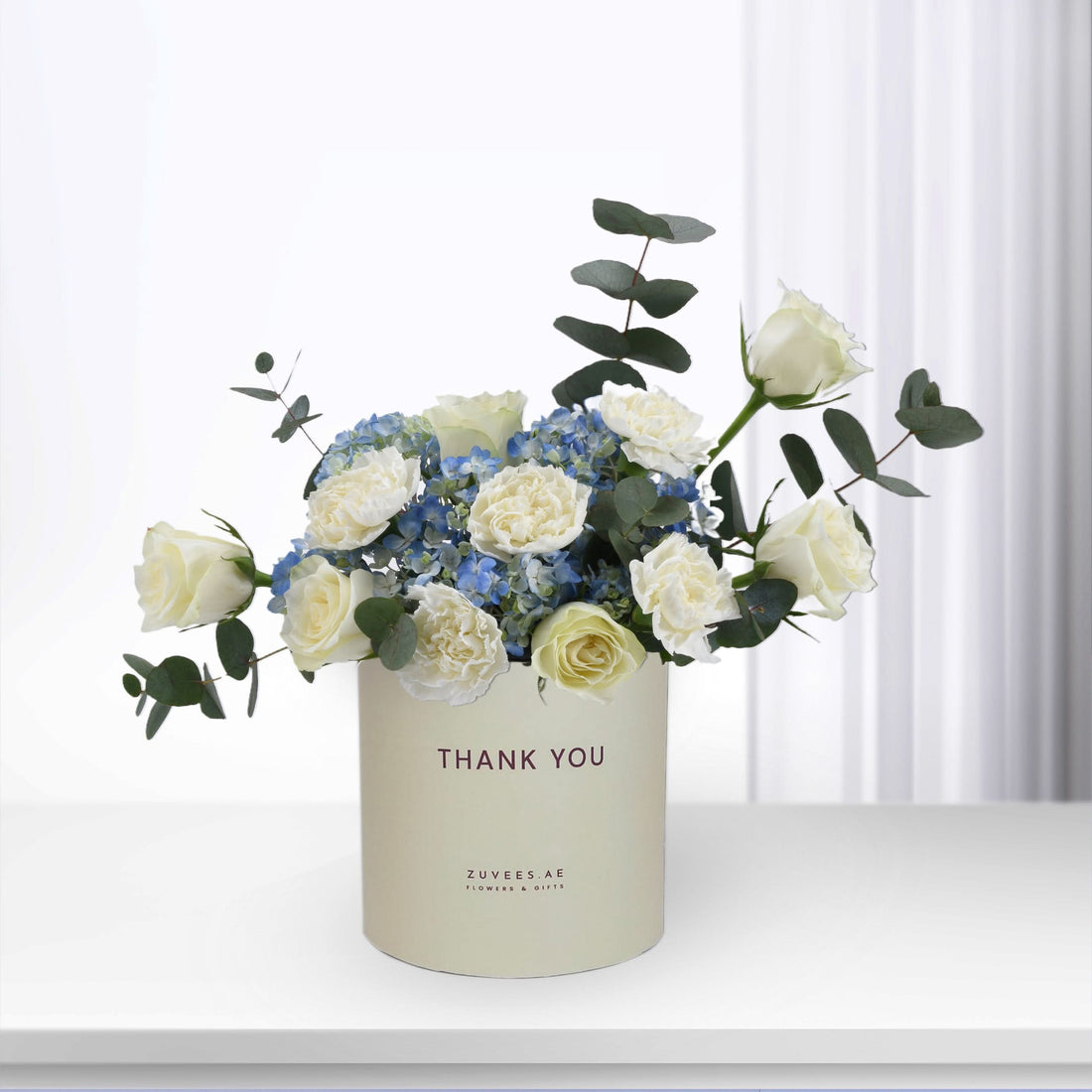 Elegant white roses and blue hydrangeas in minimalist cream "Thank You" gift box.