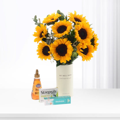 Vibrant sunflower bouquet in white vase with "Get Well Soon" text, beside honey, Strepsils, and electrolyte.
