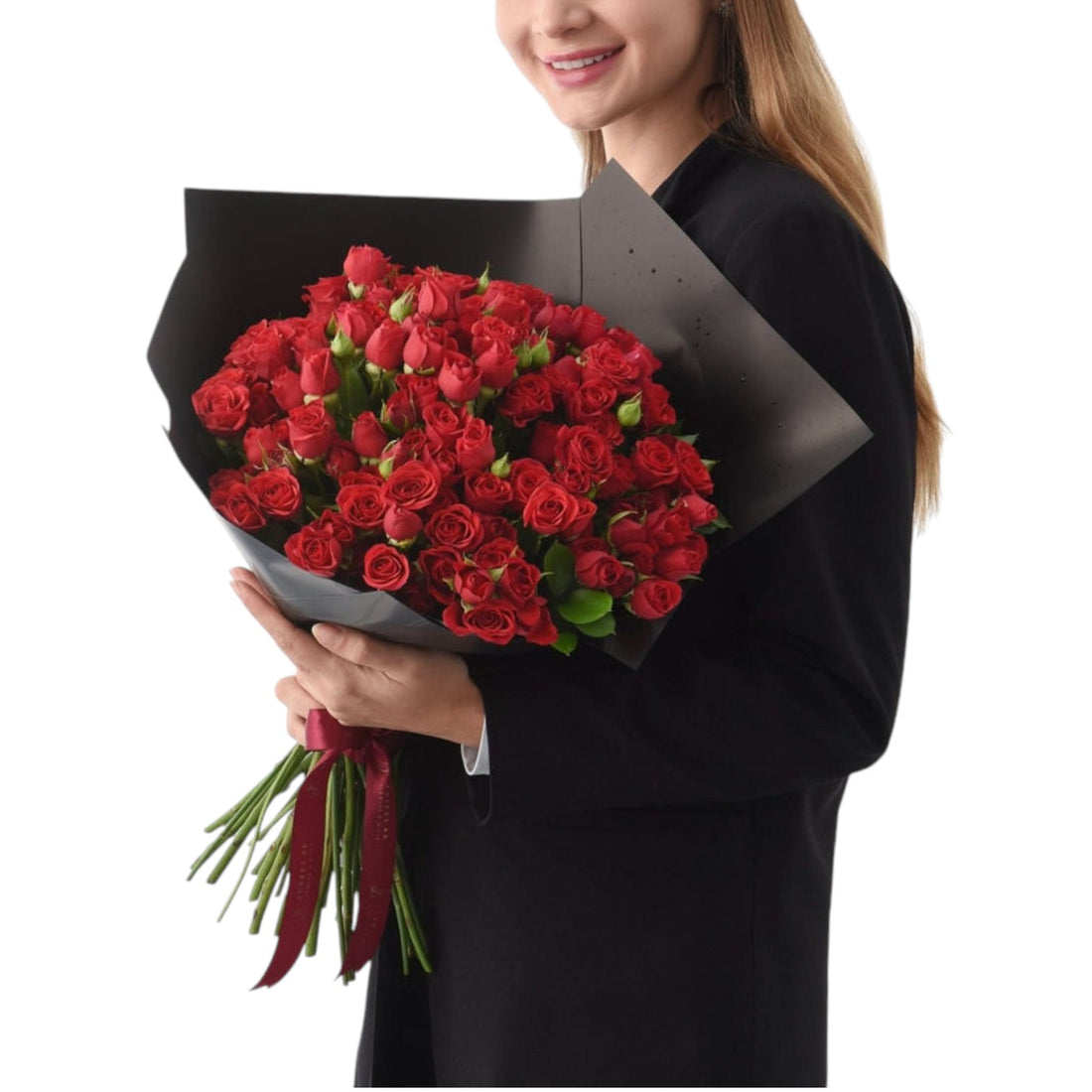 Vibrant red roses in sleek black wrap, tied with burgundy ribbon, held by smiling woman.