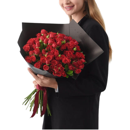 Vibrant red roses in sleek black wrap, tied with burgundy ribbon, held by smiling woman.
