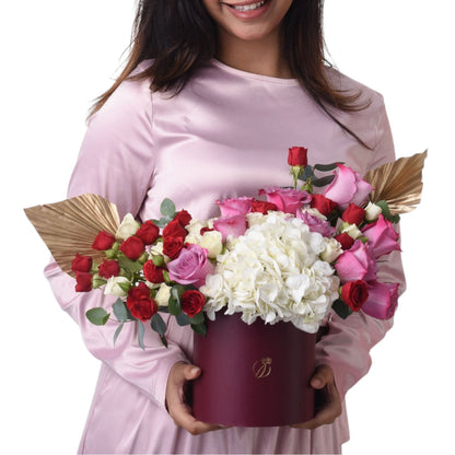 Woman holds burgundy box with red, pink, and white roses and hydrangeas.