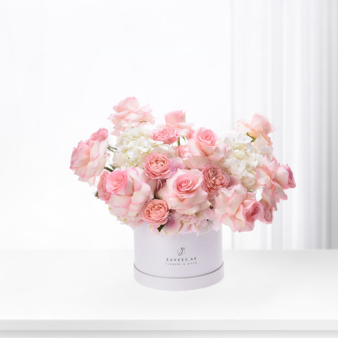 Soft pink roses and hydrangeas bloom elegantly in a branded white box.