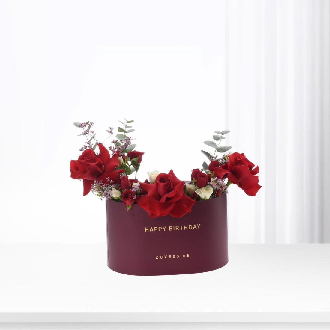 Vibrant red roses and eucalyptus in burgundy box with gold "Happy Birthday" text.