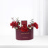 Deep burgundy box with gold "Happy Birthday" text, overflowing with vibrant red roses and delicate white blooms, accented by greenery and a "Hypnotic Poison" perfume bottle.