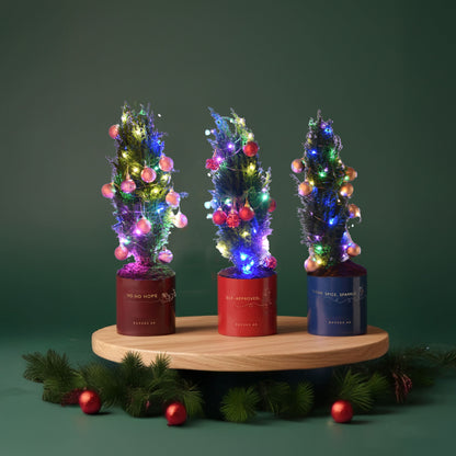Three festive mini trees glow with colorful lights in red, blue, and burgundy pots.