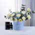 Blue box holds white roses and blue hydrangeas, beside Dior Sauvage perfume.