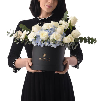Elegant white roses, blue hydrangeas, and eucalyptus in a sleek black Zuvees gift box.