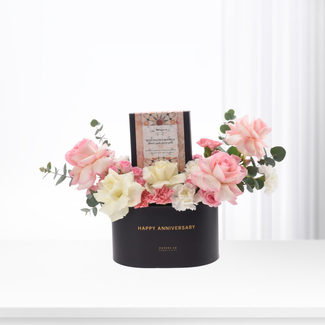 Elegant black anniversary gift box with pink roses, white blooms, and caramel chocolates.
