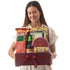 Woman smiles holding rich burgundy gift box filled with assorted treats and chocolates.