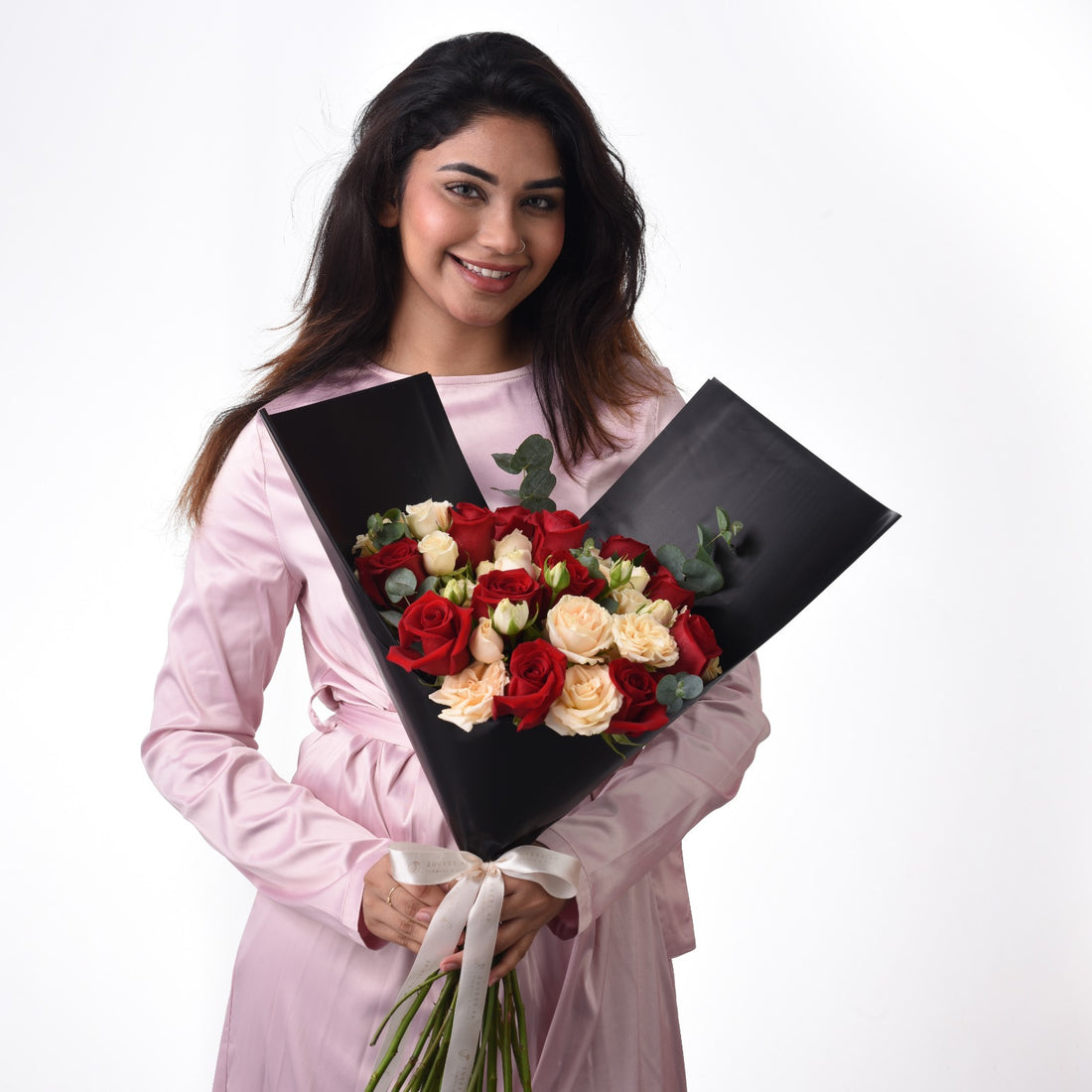 Woman in pink dress holds elegant black-wrapped bouquet of red and cream roses.