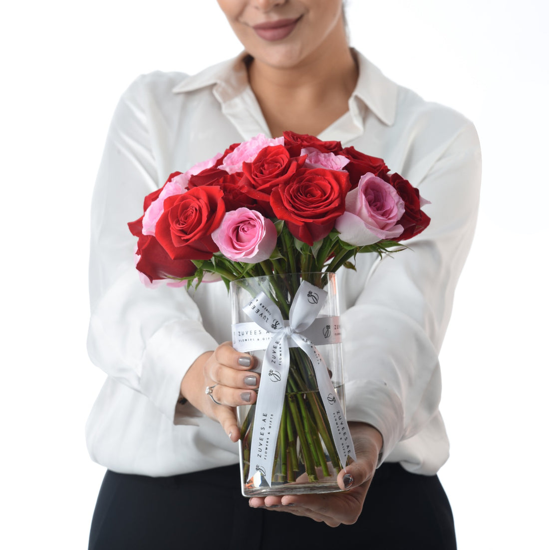 Woman holds clear vase with red and pink roses, white ribbon, and brand label.