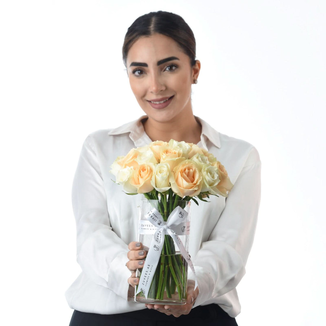 Woman holds elegant peach and cream rose bouquet in branded glass vase.